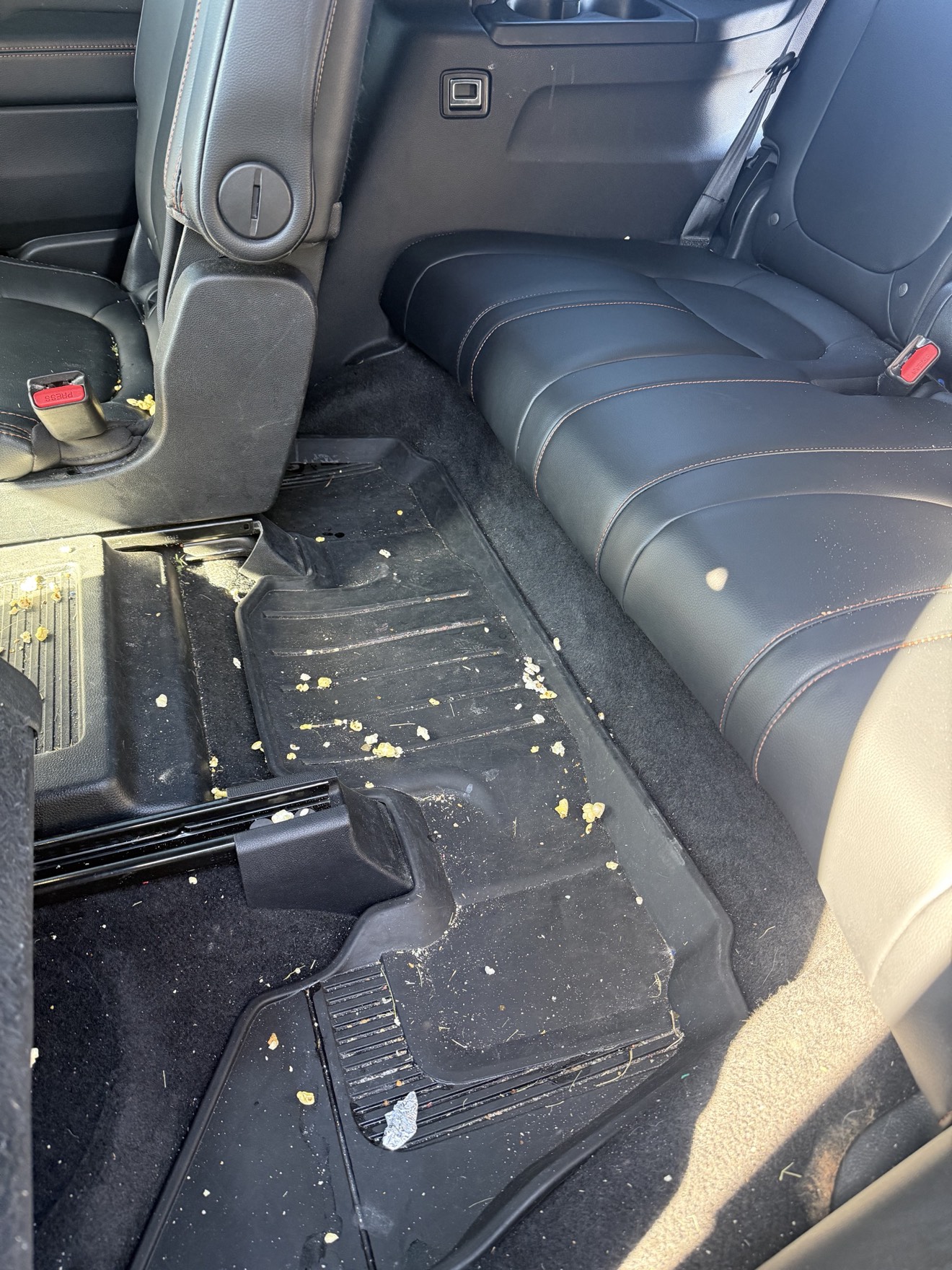 Vehicle rear floor mat and seat covered in popcorn and crumbs before a mobile detail